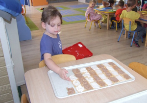 Dziewczynka układa ciastka na dużych tacach - układa je we wzór zebry.