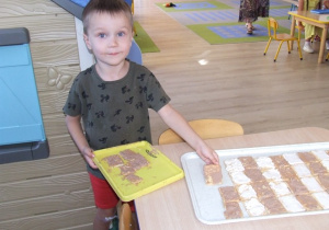 Chłopiec układa ciastka na dużych tacach - układa je we wzór zebry.
