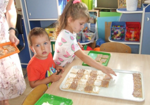 Dzieci układają ciastka na dużych tacach - układają je we wzór zebry.
