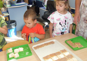 Dzieci układają ciastka na dużych tacach - układają je we wzór zebry.