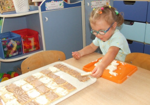 Dziewczynka układa ciastka na dużych tacach - układa je we wzór zebry.