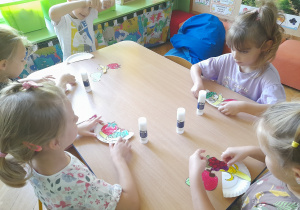 Dzieci przyklejają owoce na talerzyk papierowy.