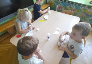 Dzieci przyklejają owoce na talerzyk papierowy.