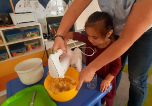 Dziewczynka z pomocą nauczycielki miksuje masło z cukrem.