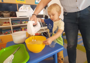 Chłopiec z pomocą nauczycielki miksuje masło z cukrem.