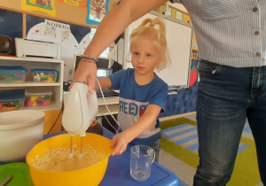 Chłopiec z pomocą nauczycielki miksuje masło z cukrem i jajkami.