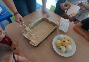 Nauczycielka rozkłada ciasto w blaszce.