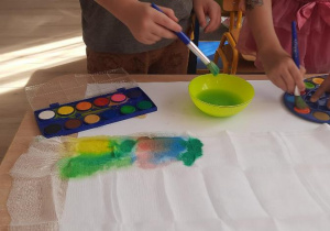 Dzieci malują po gazie pędzlem namoczonym w farbie.