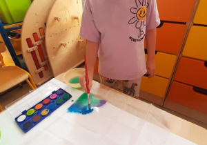 Dziecko maluje po gazie pędzlem namoczonym w farbie.