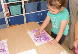 Dziewczynka zamalowuje kształty owoców.