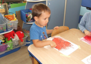 Chłopiec zamalowuje kształty owoców.
