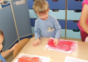Chłopiec zamalowuje kształty owoców.