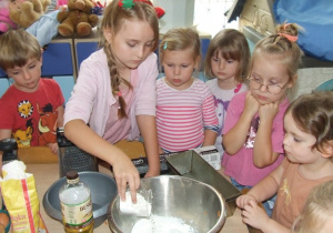 Dziewczynka wsypuje mąkę do miski.