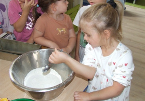 Dziewczynka wsypuje proszek do pieczenia do miski.