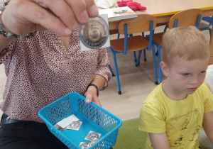 Nauczycielka pokazuje dzieciom obtazki z monetami do zabawy ruchowej.
