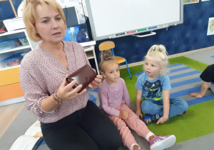 Nauczycielka pokazuje dzieciom portfel i tłumaczy do czego służy.