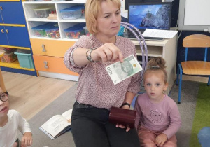 Nauczycielka pokazuje banknot 100 złotych dzieciom.