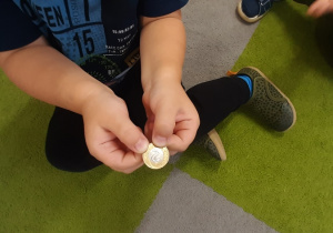 Chłopiec pokazuje w palcach monetę 2.