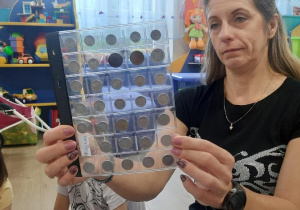 Nauczycielka pokazuje dzieciom stare monety w ablumie.