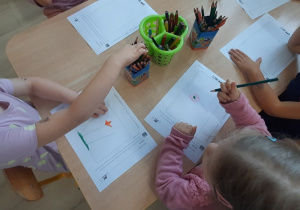 Dzieci przy stolikach projektują kartę do banlomatu.
