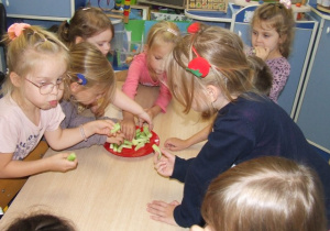 Dzieci jedzą obrane zielone ogórki.