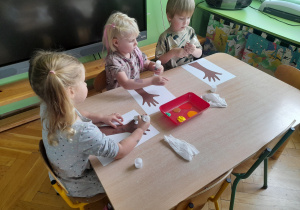 Dzieci przyklejają wycięte dłonie na kartkę papieru.