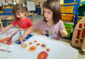 Dziewczynki malują farbami po gazie.