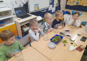 Dzieci siedzą przy stolikach i czekają na instrukcję wykonania słoika.