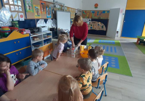 Dzieci przy stolikach słuchaja o skladnikach potrzebnych do wykonania gofrów.