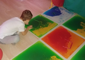 Chłopiec układa kolorowe patyczki na sensorycznych panelach.