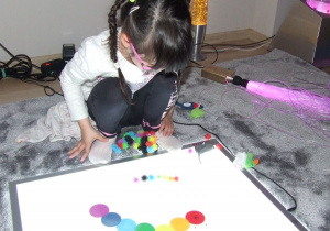 Dziewczynka układa z klocków kolorową gąsiennice wg wzoru.