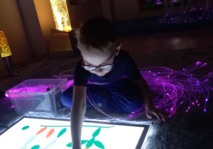 Chłopiec owinięty światłowodami, układa obrazek wykorzystując kolorowe figury.