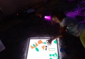 Dziewczynka układa obrazek wykorzystując kolorowe figury.