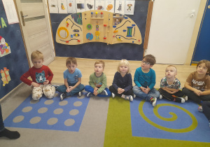 Dzieci siedzą na dywanie.
