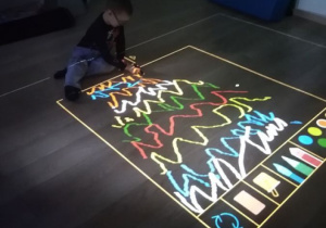 Chłopiec rysuje szalczki na podłodze interaktywnej.