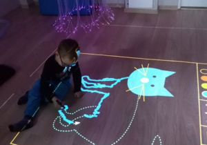Chłopiec rysuje po śladzie na podłodze interaktywnej.