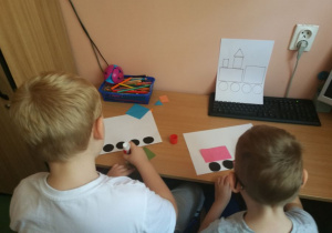 Chłopcy wyklejają rysunek z figur geometrycznych.
