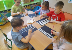 Dzieci malują białe paski farbą.