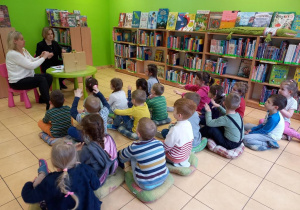 Dzieci siedzą w bibliotece i słuchają książki.