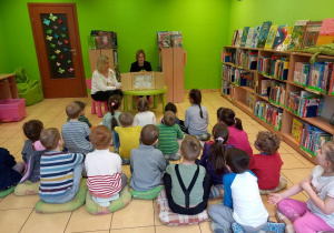 Dzieci siedzą w bibliotece i słuchają książki.