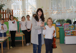 Nauczycielka przedstawia uczennicę grającą na skrzypcach.