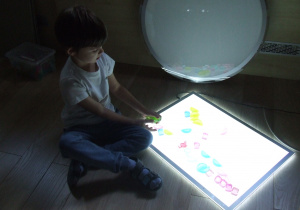 Chłopiec układa żelowe przedmioty na panelu świetlnym.
