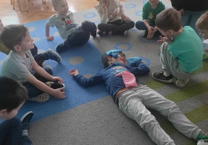 Chłopiec kładzie woreczki sensoryczne na kolegę, który leży na dywanie.
