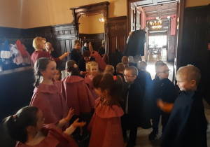 W holu pałacu, dzieci zakładają pelerynki.