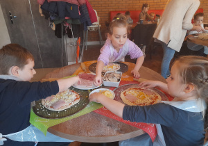 Dzieci posypują pizzę serem.
