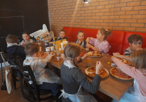 Dzieci zajadają przygotowane przez siebie pizze.