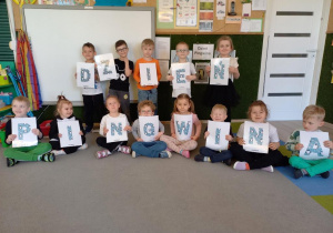 Dzieci pozują do zdjęcia z literami ułożonymi w napis - Dzień Pingwina.