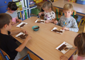 Dzieci smarują herbatniki czekoladą.