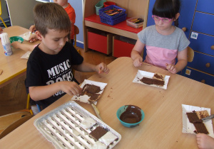 Dzieci smarują herbatniki czekoladą.