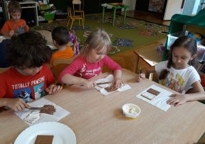 Dzieci smarują herbatniki serkiem czekoladowym.